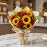 Elegante bouquet de rosas rojas y girasoles vibrantes, envuelto en papel dorado y lazo de seda, sobre mesa de mármol en flori