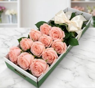Caja de 12 rosas rosadas frescas y abiertas, con un moño elegante, sobre una superficie de mármol en un entorno de floristerí