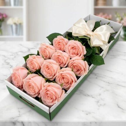 Caja de 12 rosas rosadas frescas y abiertas, con un moño elegante, sobre una superficie de mármol en un entorno de floristerí