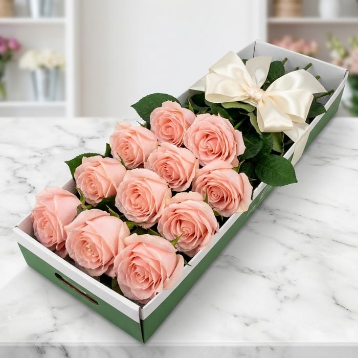 Caja de 12 rosas rosadas frescas y abiertas, con un moño elegante, sobre una superficie de mármol en un entorno de floristerí