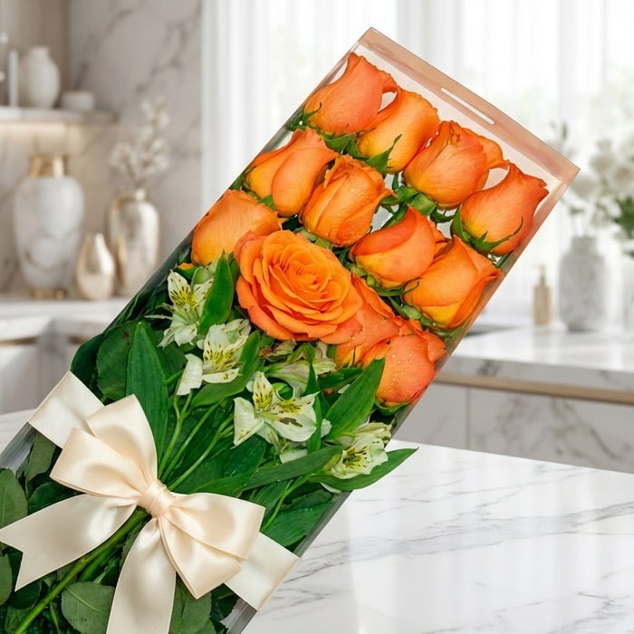 Caja de 12 rosas salmón frescas y abiertas con follaje verde y un moño elegante, sobre una superficie de mármol en un entorno