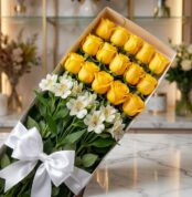 Caja de 18 rosas amarillas frescas y lirios blancos con lazo de satén blanco, sobre superficie de mármol, fondo de floristerí