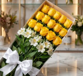 Caja de 18 rosas amarillas frescas y lirios blancos con lazo de satén blanco, sobre superficie de mármol, fondo de floristerí