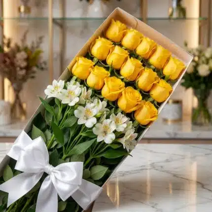 Caja de 18 rosas amarillas frescas y lirios blancos con lazo de satén blanco, sobre superficie de mármol, fondo de floristerí