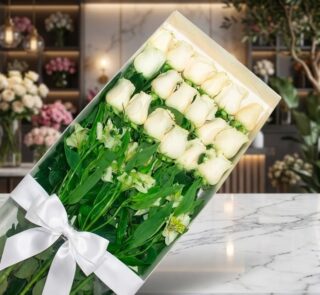 Caja transparente con 18 rosas blancas frescas y alstroemerias, atada con un moño blanco, sobre una superficie de mármol en u