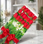 Caja transparente con 18 rosas rojas frescas y alstroemerias blancas, atada con un elegante moño rojo, sobre una superficie d