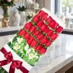 Caja de 24 rosas rojas frescas y abiertas con alstroemerias blancas, moño de satén rojo, sobre mármol pulido en floristería p