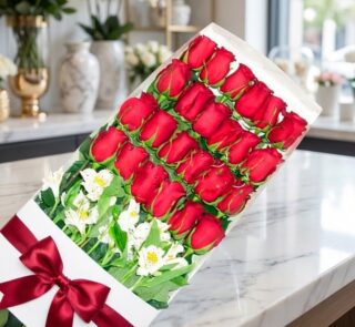 Caja de 24 rosas rojas frescas y abiertas con alstroemerias blancas, moño de satén rojo, sobre mármol pulido en floristería p