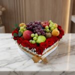 Caja Armani con arreglo de frutas frescas y rosas rojas vibrantes en forma de corazón, sobre mármol blanco.