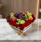 Caja Armani con arreglo de frutas frescas y rosas rojas vibrantes en forma de corazón, sobre mármol blanco.