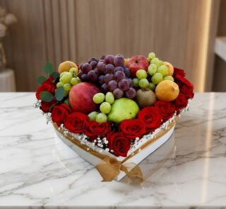 Caja Armani con arreglo de frutas frescas y rosas rojas vibrantes en forma de corazón, sobre mármol blanco.