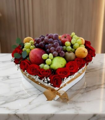 Caja Armani con arreglo de frutas frescas y rosas rojas vibrantes en forma de corazón, sobre mármol blanco.