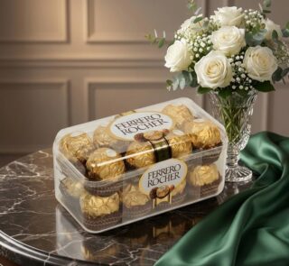 Caja de 16 chocolates Ferrero Rocher sobre mesa de mármol, acompañada de un ramo de rosas blancas y follaje en un jarrón de c