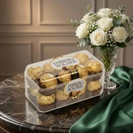 Caja de 16 chocolates Ferrero Rocher sobre mesa de mármol, acompañada de un ramo de rosas blancas y follaje en un jarrón de c