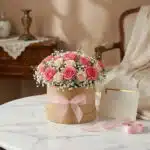 Caja floral GIADA con 12 rosas frescas rosadas y crema, gypsophila, cinta de satén rosa y tarjeta de regalo en un entorno ele