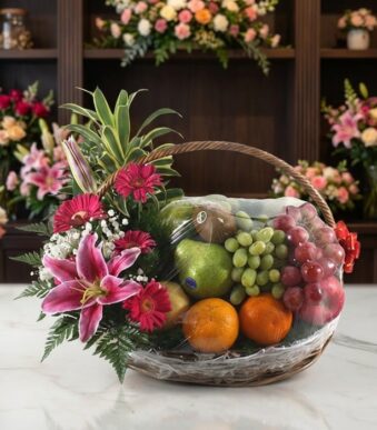 Canasta Frutal CARMINE con lirios rosados, gerberas fucsia, follaje verde y frutas frescas como uvas, manzanas, naranjas y ki