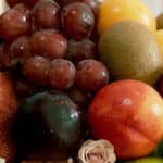 Primer plano extremo de uvas rojas, kiwi, durazno y ciruela con gotas de rocío, destacando la frescura y textura de la Canast