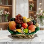 Canasta de frutas Corvus con uvas rojas, manzanas, kiwis y duraznos, sobre una superficie de mármol en un entorno de floriste