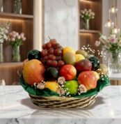 Canasta de frutas Corvus con uvas rojas, manzanas, kiwis y duraznos, sobre una superficie de mármol en un entorno de floriste