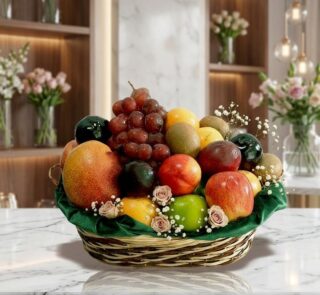 Canasta de frutas Corvus con uvas rojas, manzanas, kiwis y duraznos, sobre una superficie de mármol en un entorno de floriste