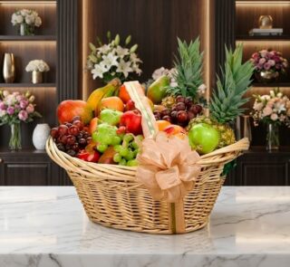 Canasta de mimbre con frutas gourmet variadas: piñas, uvas, manzanas, peras, mangos y plátanos, sobre mármol blanco en floris