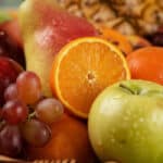 Primer plano extremo de una canasta de frutas Hydra con naranja, manzana verde, uvas y pera, mostrando texturas hiperrealista