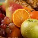 Primer plano extremo de una canasta de frutas Hydra con naranja, manzana verde, uvas y pera, mostrando texturas hiperrealista