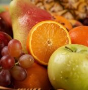 Primer plano extremo de una canasta de frutas Hydra con naranja, manzana verde, uvas y pera, mostrando texturas hiperrealista