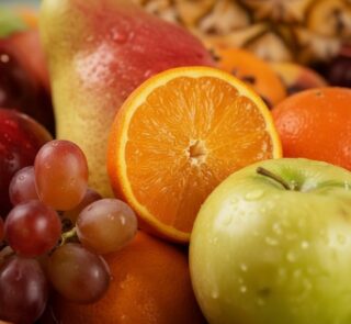 Primer plano extremo de una canasta de frutas Hydra con naranja, manzana verde, uvas y pera, mostrando texturas hiperrealista