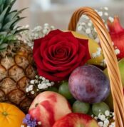 Primer plano extremo de una rosa roja vibrante con gotas de rocío, rodeada de frutas frescas como piña, uvas, ciruela y manza