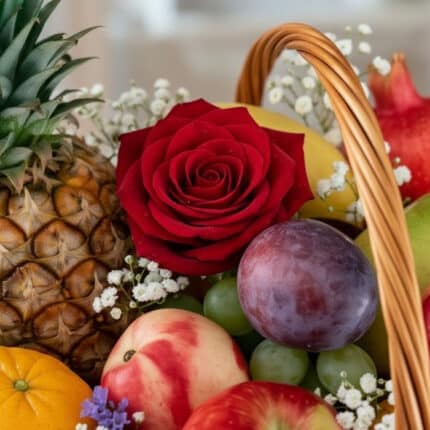 Primer plano extremo de una rosa roja vibrante con gotas de rocío, rodeada de frutas frescas como piña, uvas, ciruela y manza