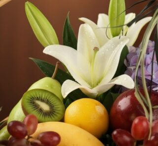 Primer plano extremo de una canasta de frutas premium con lirios blancos, kiwi, uvas, manzana, pera, limón y mango, con gotas