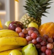 Primer plano extremo de una canasta de frutas Sirio con uvas rojas, peras verdes, plátanos amarillos, manzanas y piña, destac