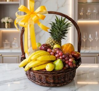 Canasta de mimbre con frutas frescas variadas como piña, plátanos, uvas, manzanas y peras, adornada con un lazo amarillo bril