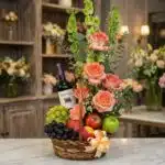 Canasta gourmet CAPRICE con rosas frescas color salmón, uvas verdes y moradas, manzanas rojas y verdes, duraznos y una botell