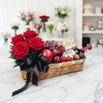Elegante cesta de regalo con rosas rojas frescas, vino tinto, chocolates Ferrero Rocher y una selección de frutas variadas co