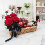 Elegante cesta de regalo con rosas rojas frescas, vino tinto, chocolates Ferrero Rocher y una selección de frutas variadas co