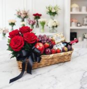 Elegante cesta de regalo con rosas rojas frescas, vino tinto, chocolates Ferrero Rocher y una selección de frutas variadas co