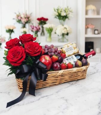 Elegante cesta de regalo con rosas rojas frescas, vino tinto, chocolates Ferrero Rocher y una selección de frutas variadas co