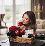 Mujer elegante admirando una rosa roja de la CestaANGELO, que incluye rosas, manzanas, vino y chocolates Ferrero Rocher, en u