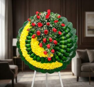 Corona fúnebre Adela con rosas rojas y flores blancas sobre base de crisantemos amarillos y hojas verdes, en sala de velación