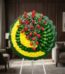 Corona fúnebre Adela con rosas rojas y flores blancas sobre base de crisantemos amarillos y hojas verdes, en sala de velación