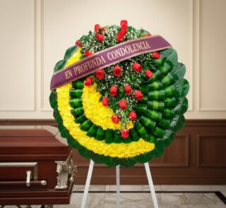 Corona fúnebre Adela con rosas rojas y flores amarillas, cinta morada 'En Profunda Condolencia', junto a un ataúd en sala de