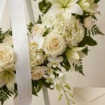 Fotografía macro premium de la Corona Fúnebre Almudena, con rosas, lirios y orquídeas blancas, follaje verde, rocío sutil y c