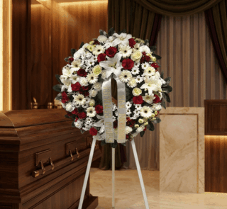 Corona de flores fúnebres Ararat con rosas rojas, lirios blancos y margaritas, junto a un ataúd de madera en un ambiente eleg