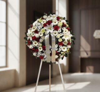 Corona de homenaje fúnebre Ararat con flores blancas y rojas, lirios, rosas y margaritas, sobre un trípode en una sala de vel