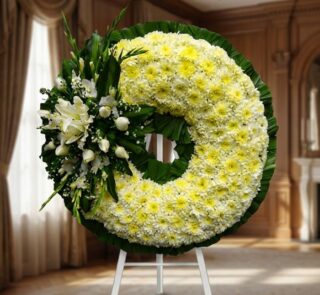 Corona fúnebre Bethesda con crisantemos blancos y lirios, en una sala de velación premium con luz natural suave y bokeh.