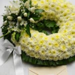 Fotografía macro premium de la Corona Fúnebre Bethesda, mostrando texturas hiperrealistas de pétalos blancos y follaje verde