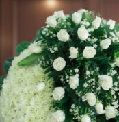Fotografía macro premium de la Corona Fúnebre Descansa en Paz, mostrando rosas blancas y follaje verde con rocío sutil, profu