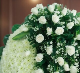 Fotografía macro premium de la Corona Fúnebre Descansa en Paz, mostrando rosas blancas y follaje verde con rocío sutil, profu